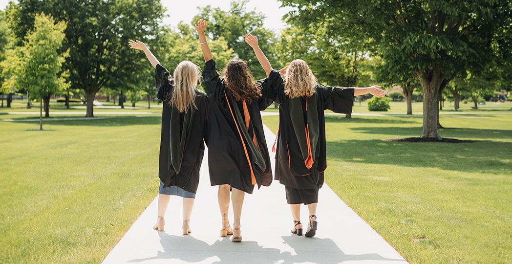 photo of 3 pharmacy students with their caps and gowns on walking on campus
